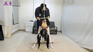 Eine junge asiatische Schönheit wird in einer intensiven BDSM-Szene geknebelt und gefesselt.