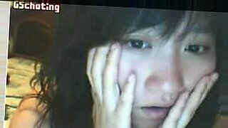 Eine asiatische Frau erkundet ihre enge Muschi mit ihrem Daumen vor der Kamera.
